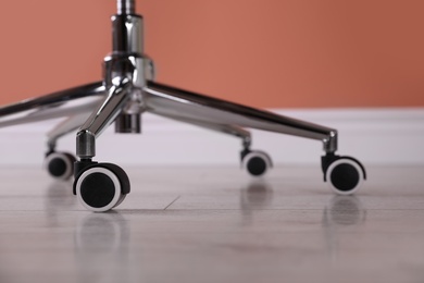 Photo of Modern office chair with wheels on wooden floor, closeup