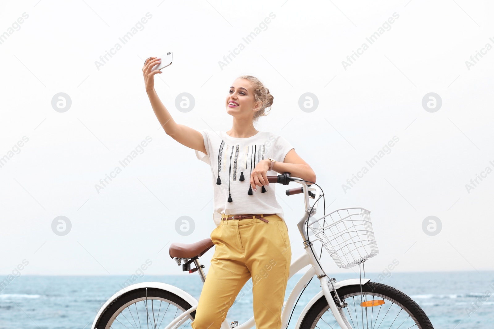 Photo of Attractive woman taking selfie near bicycle on sea coast