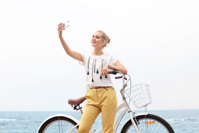 Attractive woman taking selfie near bicycle on sea coast