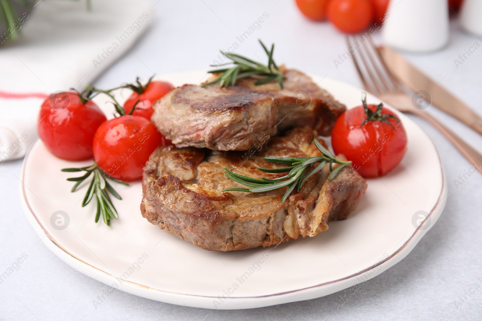 Photo of Delicious fried meat with rosemary and tomatoes on white table, closeup