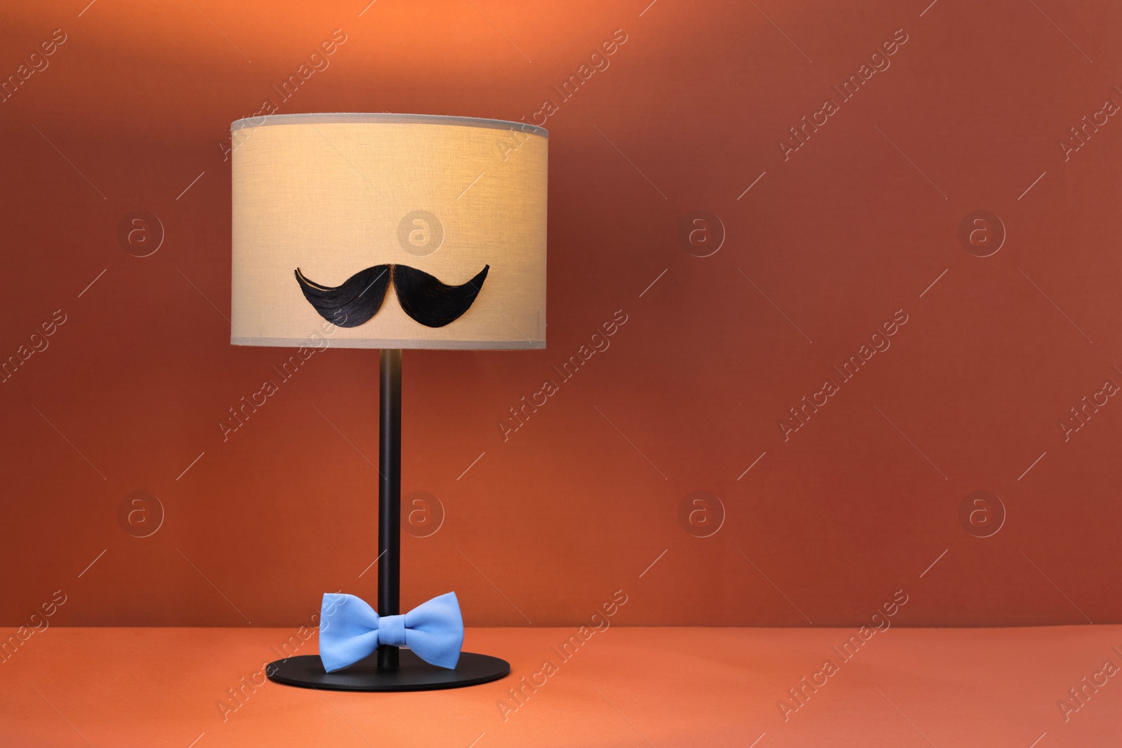 Photo of Man's face made of artificial mustache, bow tie and lamp on terracotta background. Space for text