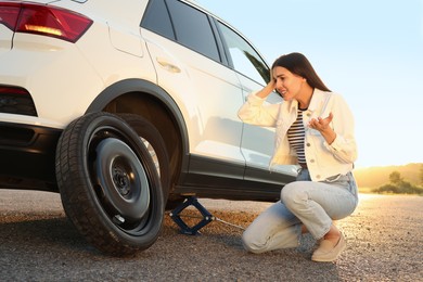 Photo of Worried young woman near car on roadside. Changing wheel