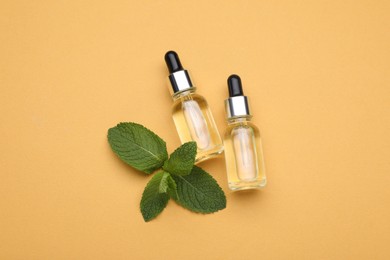 Bottles of essential oil and mint on pale orange background, flat lay