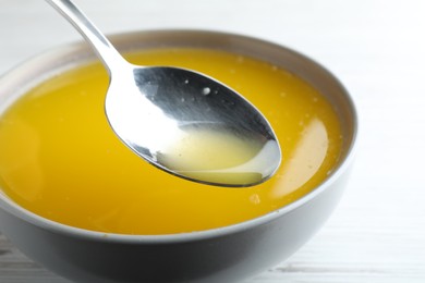Photo of Spoon of clarified butter over bowl on white table, closeup