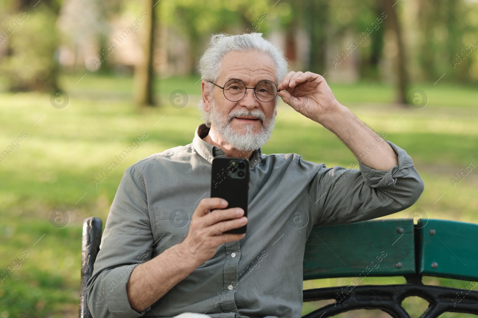 Photo of Portrait of happy grandpa with glasses using smartphone on bench in park