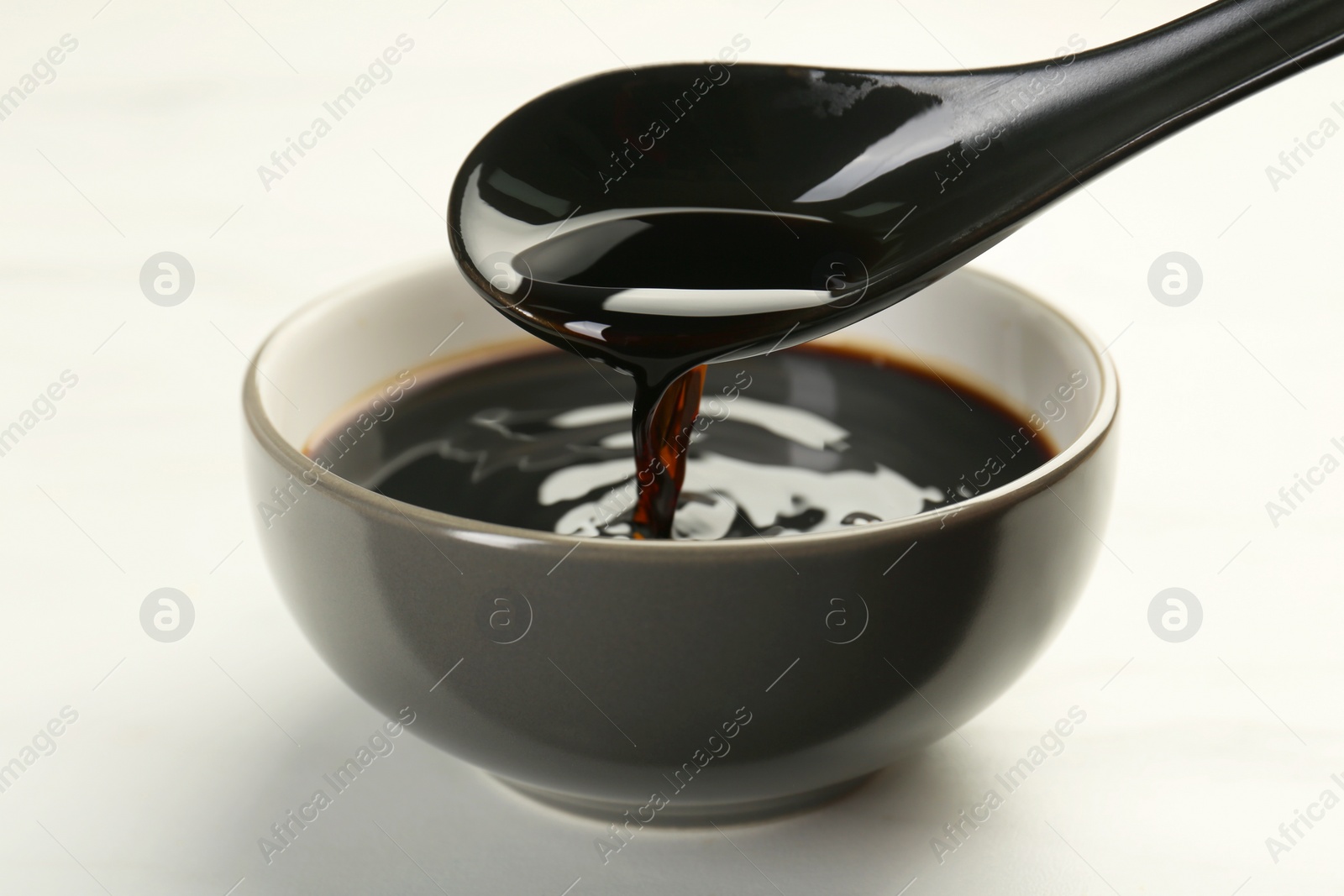 Photo of Taking soy sauce with spoon from bowl at white table, closeup