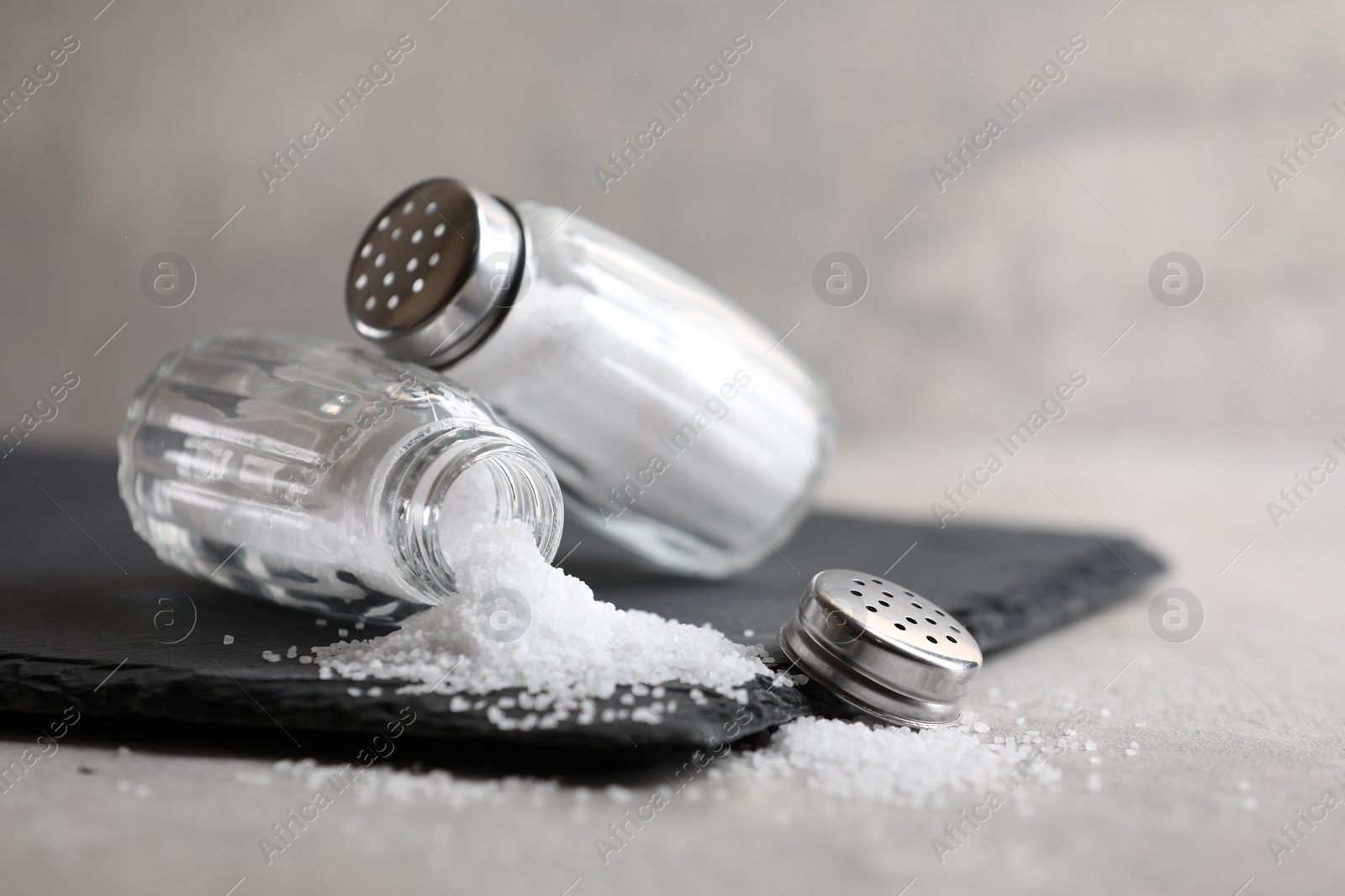 Photo of Natural salt in shakers on grey table, closeup. Space for text