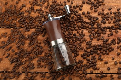 Photo of Modern manual coffee grinder with beans on wooden table, flat lay