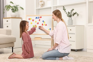 Mom teaching her daughter alphabet with magnetic letters at home