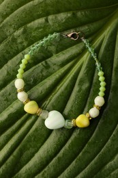 Beautiful bracelet with gemstones on green leaf, top view