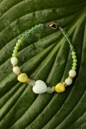 Photo of Beautiful bracelet with gemstones on green leaf, top view