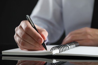 Photo of Man writing in notebook at black table, closeup. Space for text