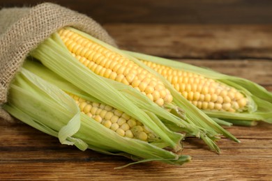 Photo of Fresh corncobs with green husks on wooden table, closeup