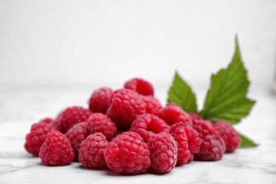Photo of Fresh ripe raspberries with green leaves on white marble table, closeup