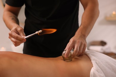 Therapist giving fire cupping treatment to patient indoors, closeup