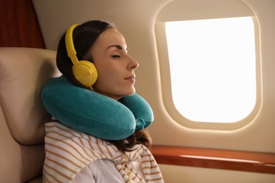 Photo of Young woman with travel pillow resting while listening to music in airplane during flight
