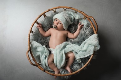 Photo of Cute newborn baby in wicker basket on grey background, top view