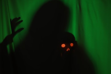 Silhouette of creepy ghost with skull behind dark green cloth