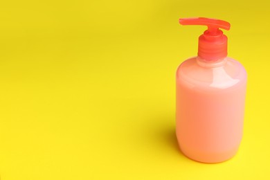 Bottle of liquid soap on yellow background, space for text