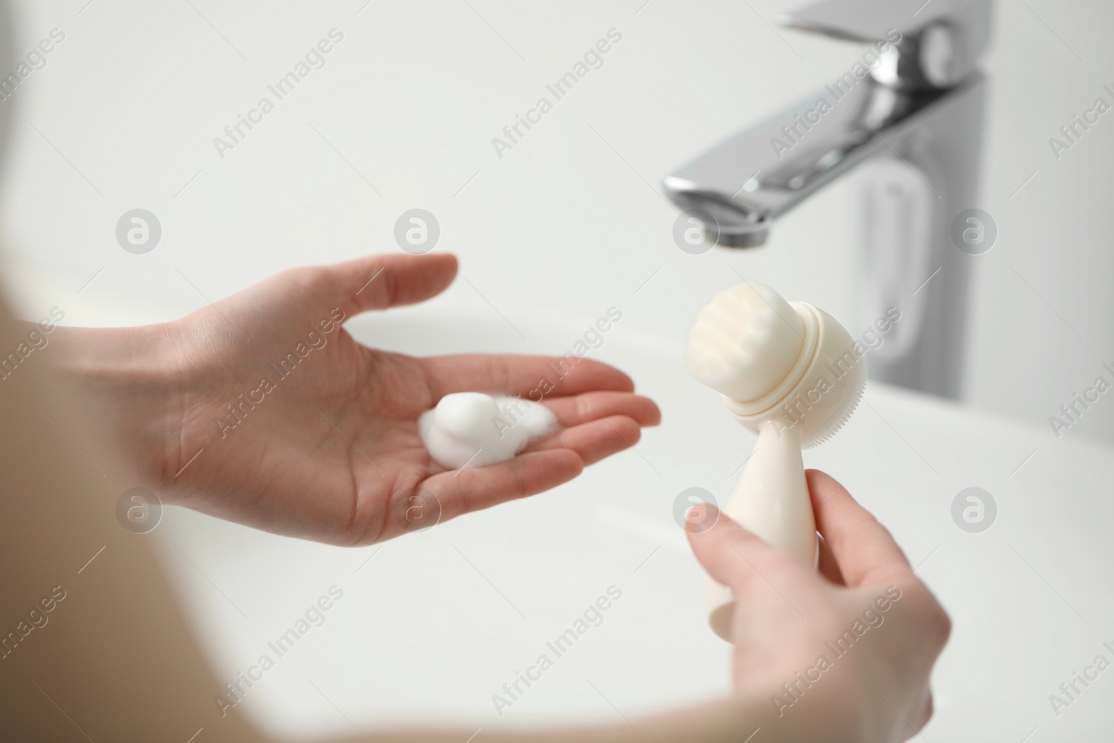 Photo of Washing face. Woman with brush and cleansing foam above sink in bathroom, closeup