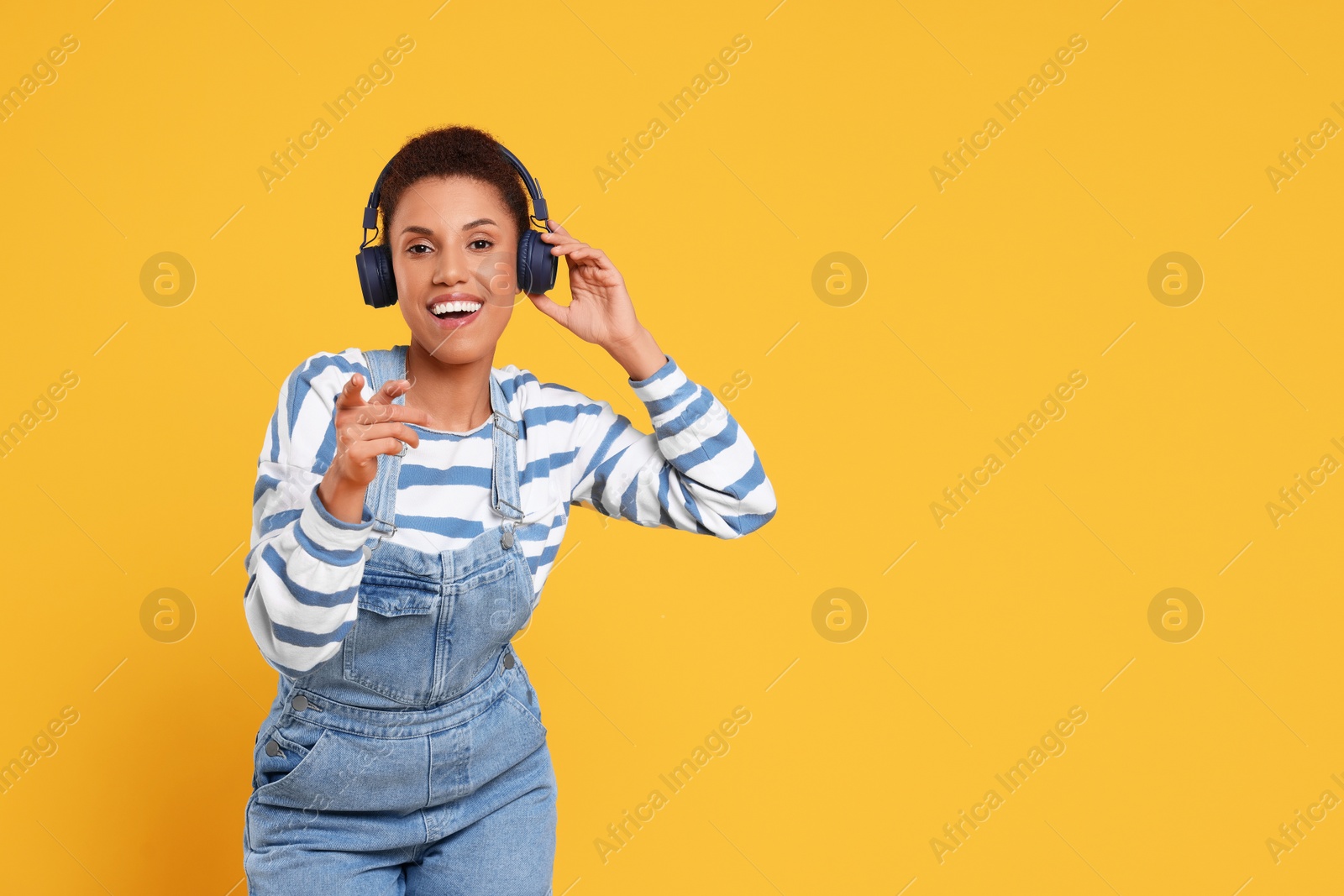 Photo of Happy young woman in headphones dancing on orange background. Space for text