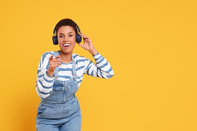 Happy young woman in headphones dancing on orange background. Space for text