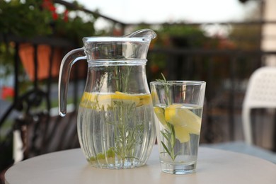 Photo of Jug and glass with refreshing lemon water on light table outdoors