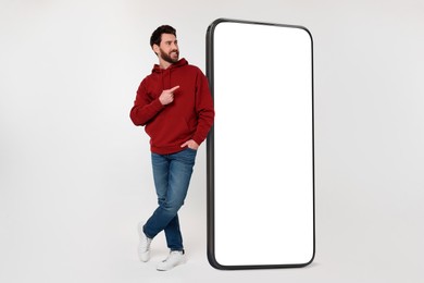 Image of Man pointing at huge mobile phone with empty screen on grey background. Mockup for design