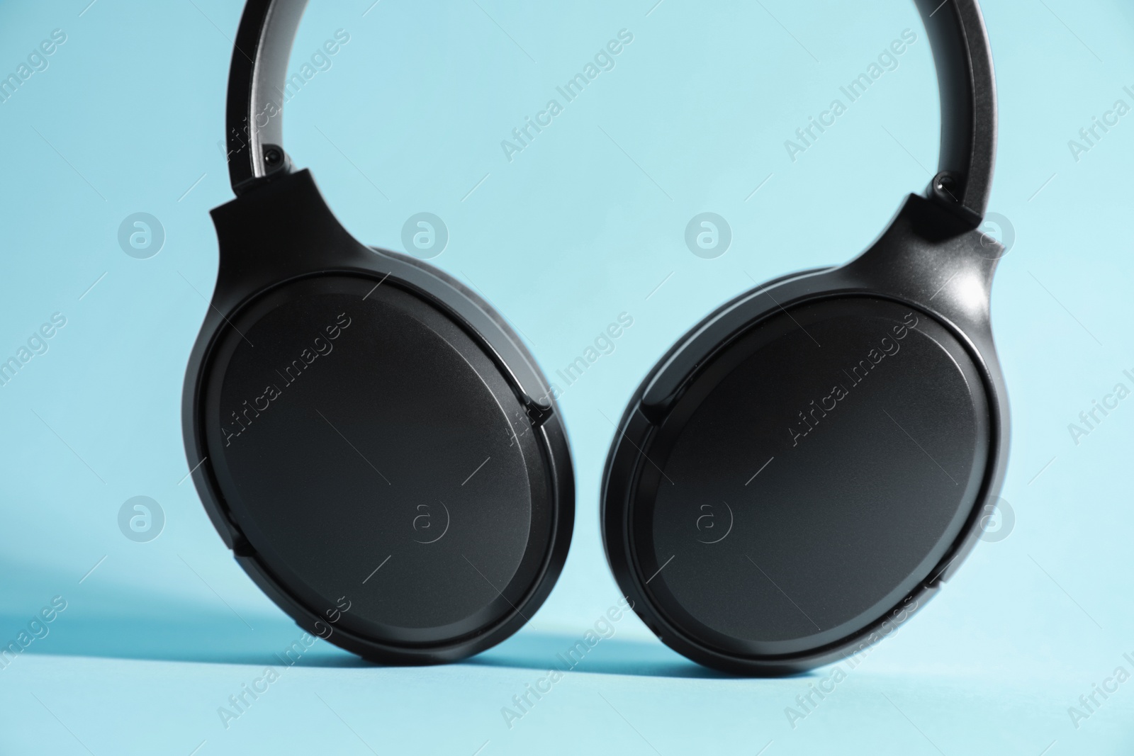 Photo of Modern wireless headphones on light blue background, closeup