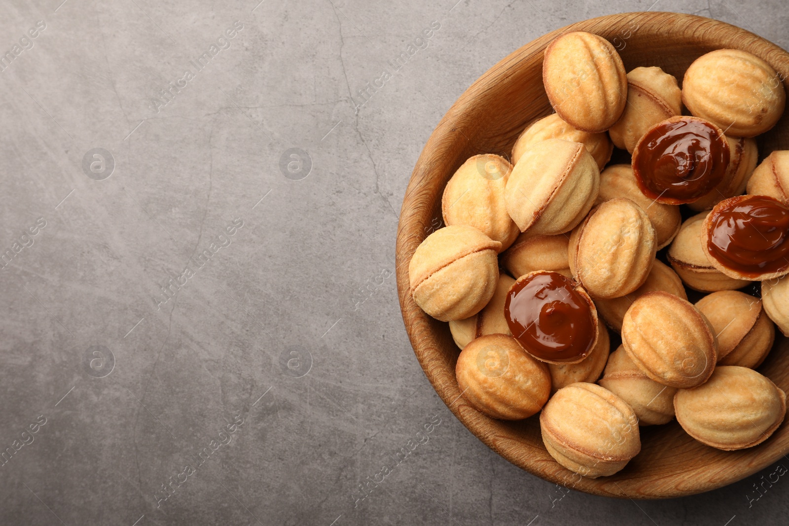 Photo of Delicious nut shaped cookies with boiled condensed milk in wooden bowl on gray textured table, top view. Space for text