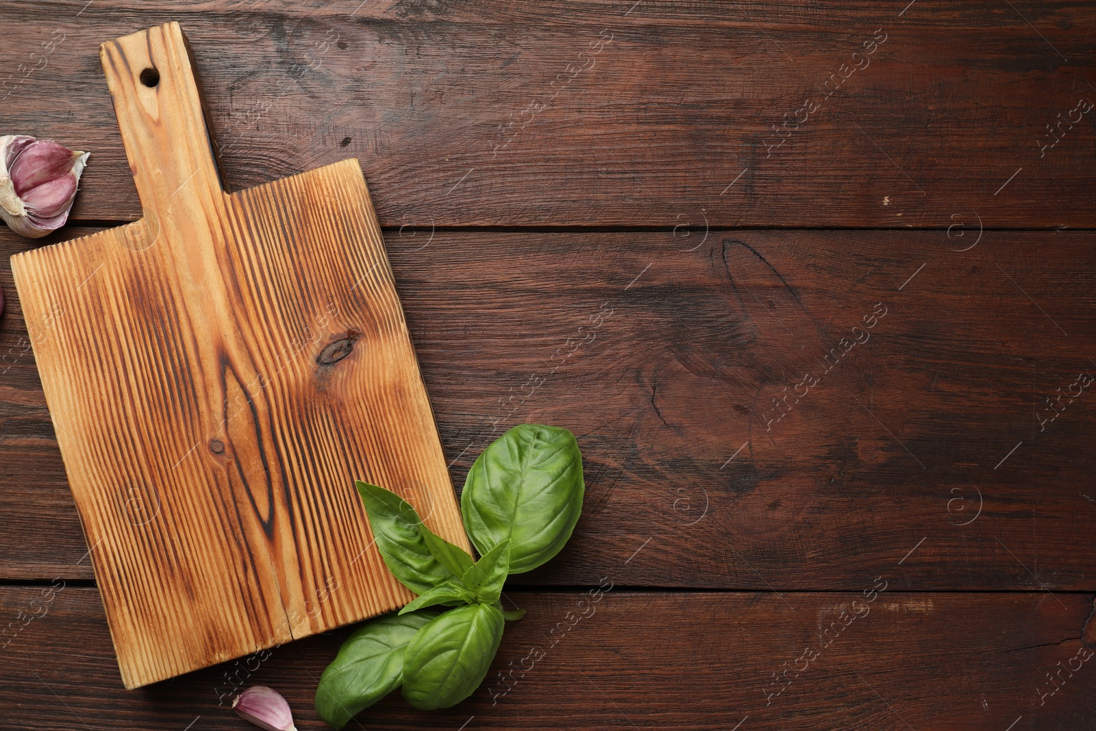 Photo of Cutting board, basil and garlic on wooden table, flat lay. Space for text