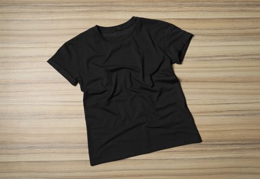 Stylish black T-shirt on wooden table, top view