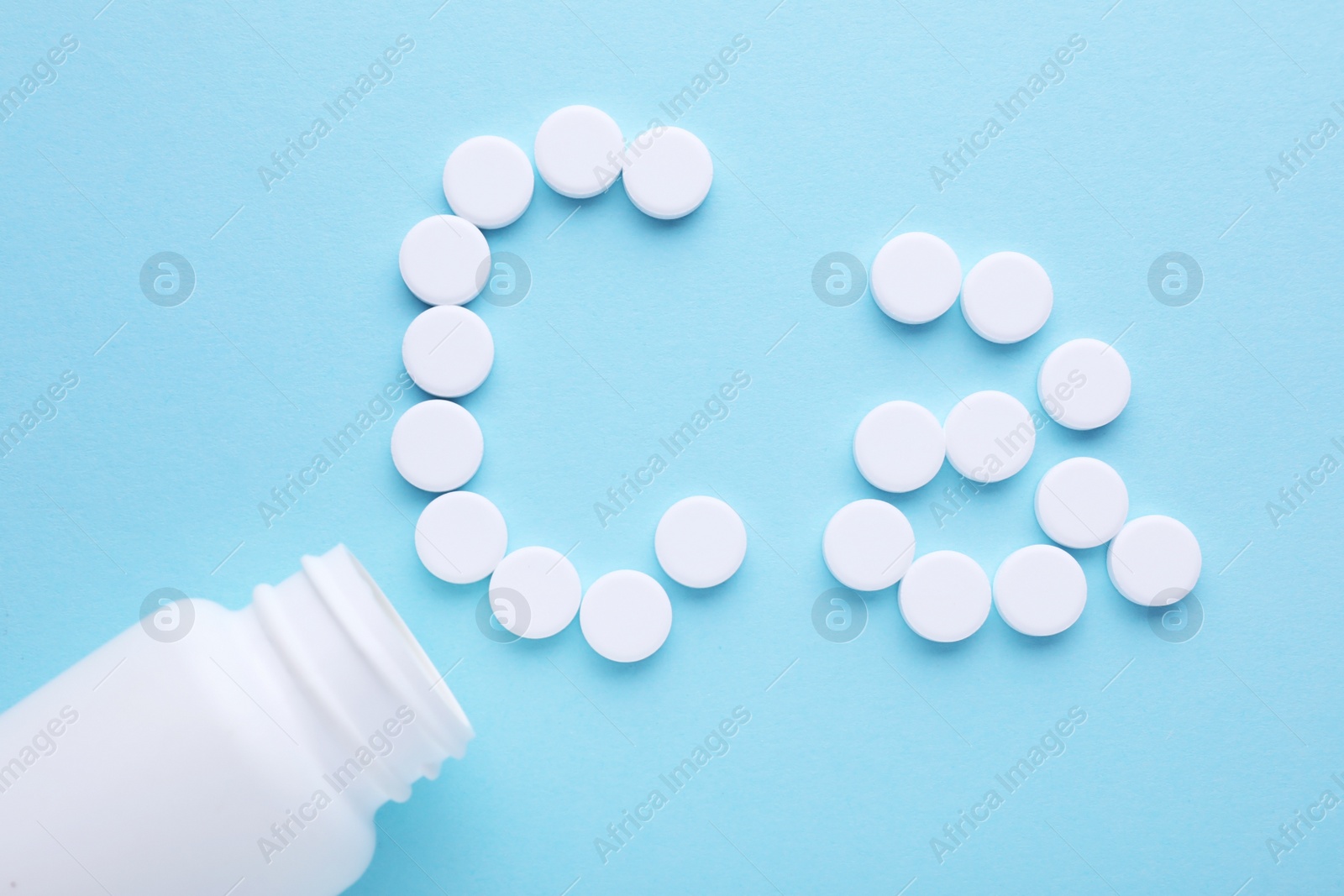 Photo of Open bottle and calcium symbol madewhite pills on light blue background, flat lay