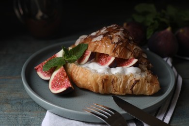 Photo of Delicious croissant with figs and cream served on light blue wooden table, closeup