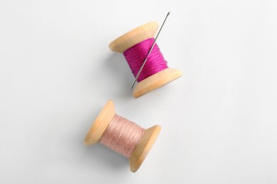 Colorful sewing threads with needle on white background, top view