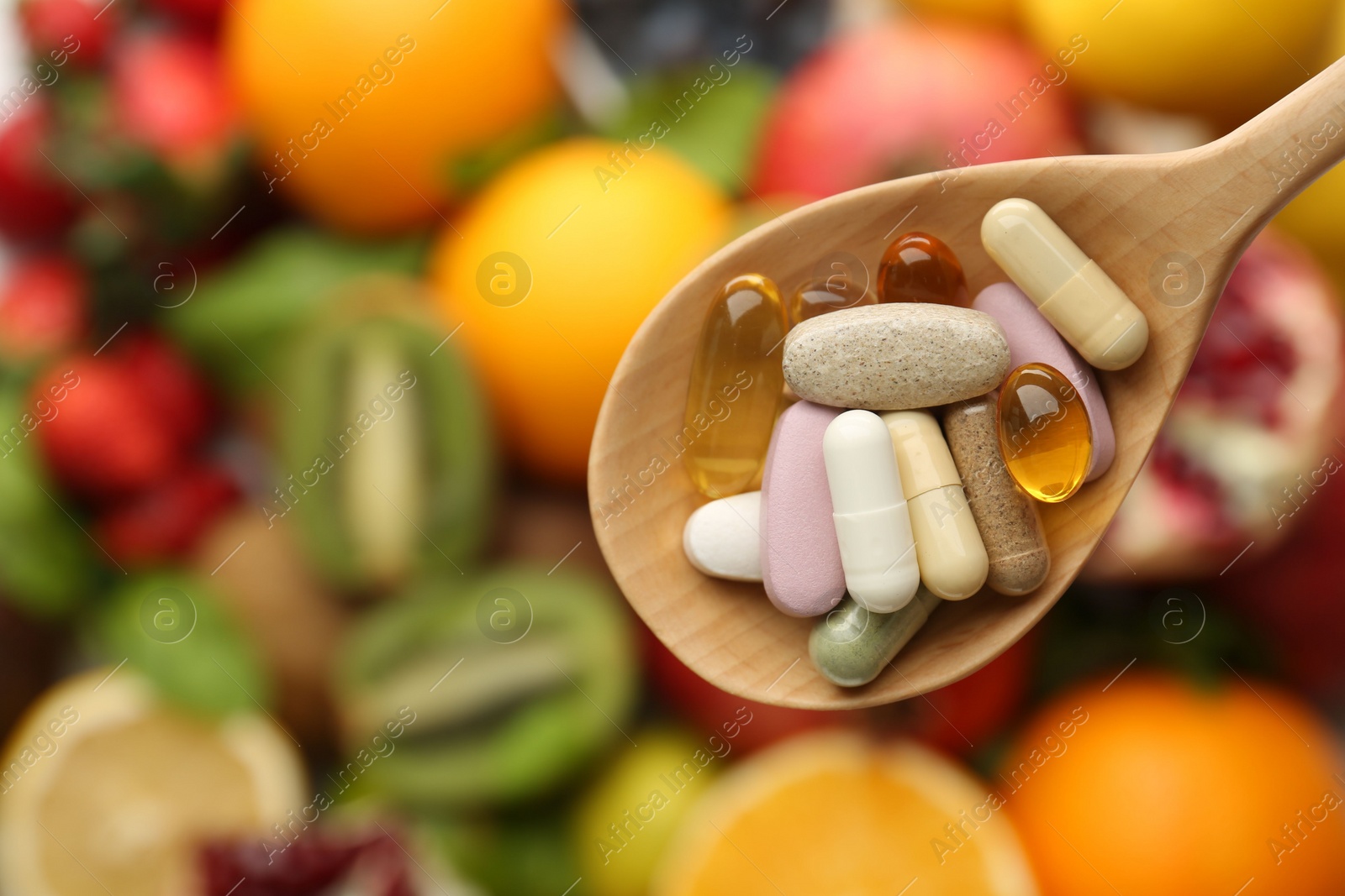 Photo of Different vitamin pills in spoon over fresh fruits, top view. Space for text