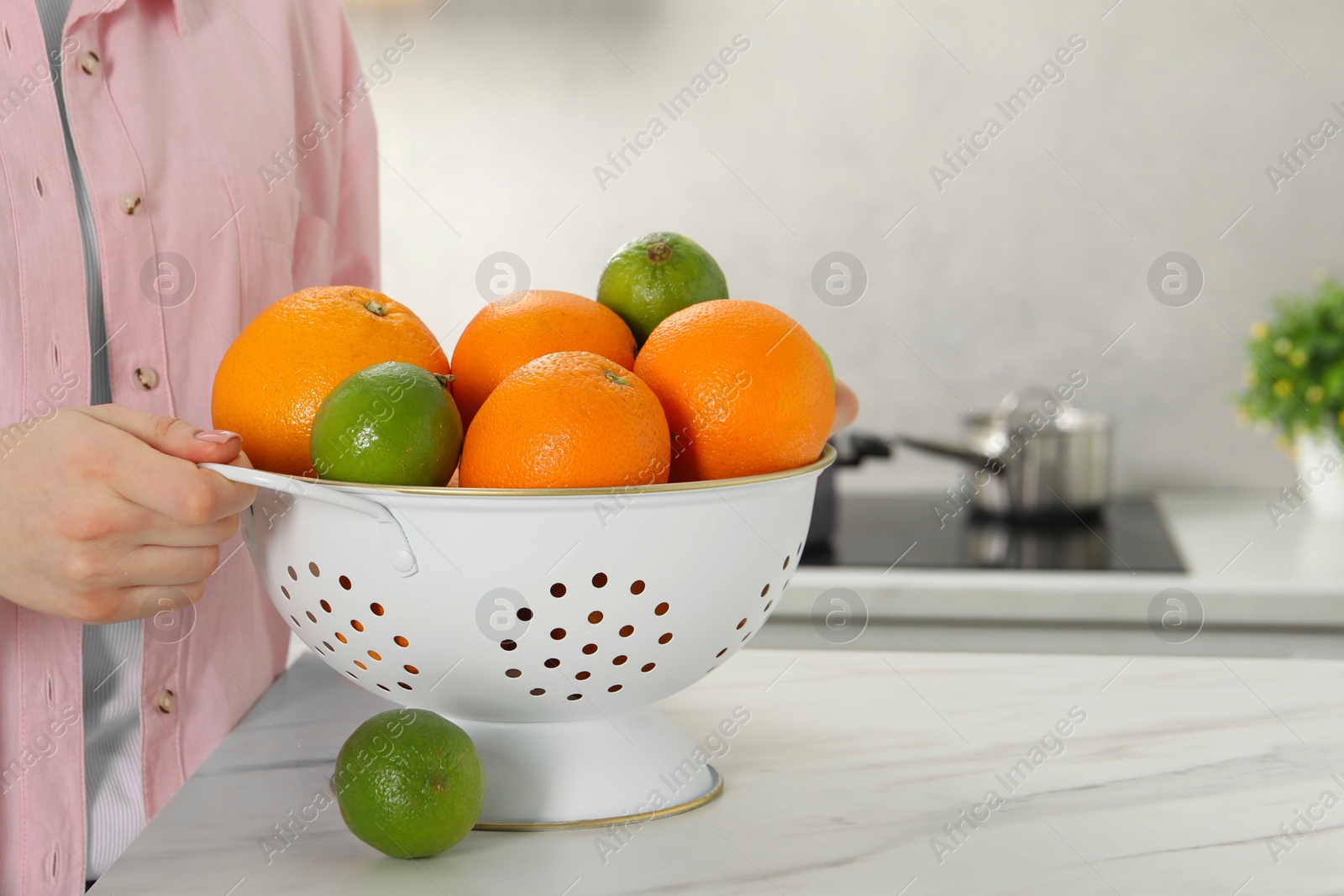 Photo of Woman holding colander with fresh fruits at white marble table in kitchen, closeup. Space for text