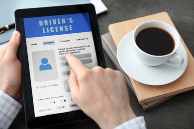 Man using tablet to fill driver's license application form at grey table, closeup