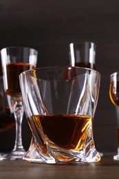 Different delicious liqueurs in glasses on wooden table, closeup