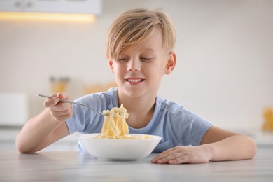 Photo of Happy boy eating tasty pasta at table in kitchen