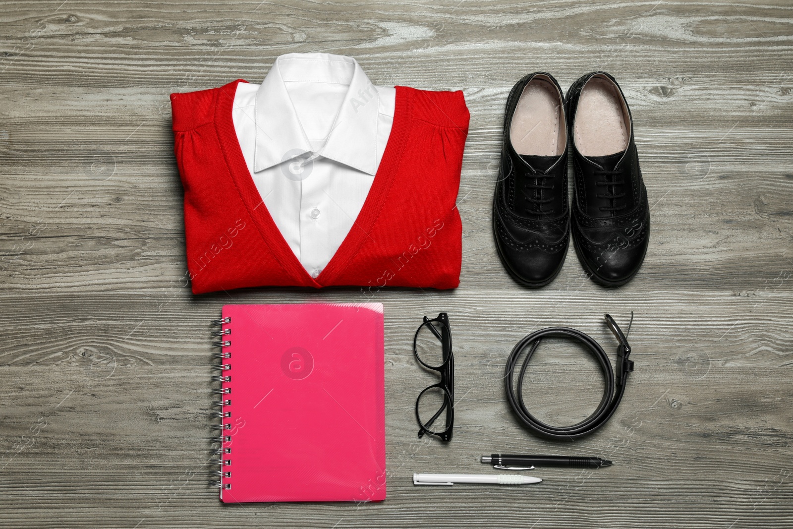 Photo of Stylish school uniform for girl, glasses and stationery on wooden background, flat lay