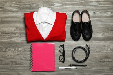 Stylish school uniform for girl, glasses and stationery on wooden background, flat lay