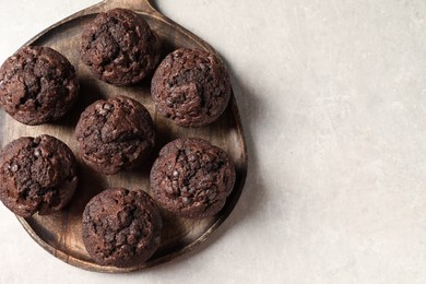 Photo of Board with delicious chocolate muffins on light table, top view. Space for text