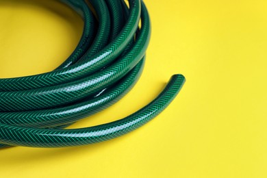 Photo of Green rubber watering hose on yellow background, closeup. Space for text