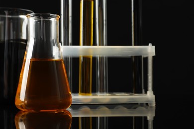 Photo of Laboratory glassware with different types of oil on black background, closeup