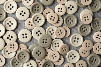 Many plastic sewing buttons on grey fabric, flat lay