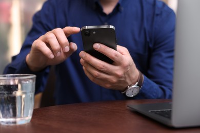 Photo of Man sending message via smartphone at table indoors, closeup