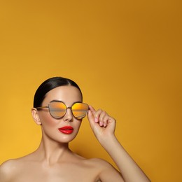 Attractive woman in stylish sunglasses on orange background, space for text. Sea sunset reflecting in lenses