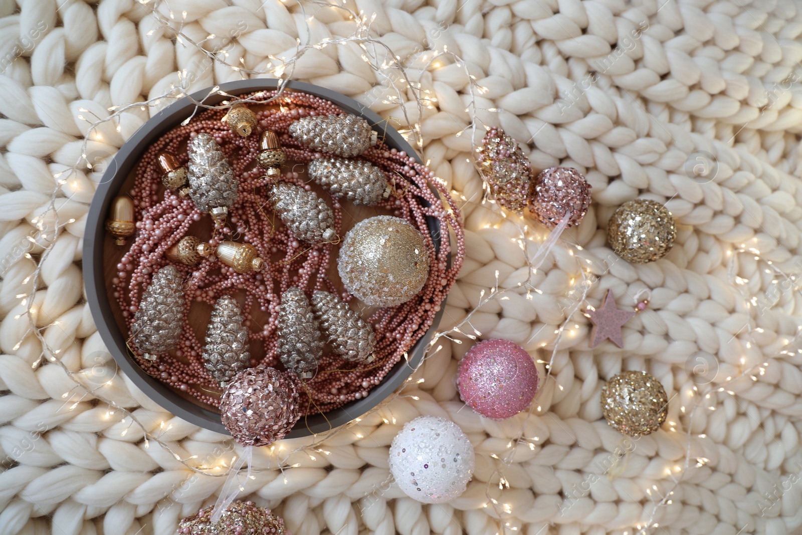 Photo of Beautiful Christmas tree baubles and fairy lights on white knitted fabric, above view