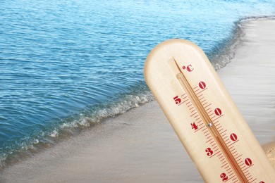 Closeup view of weather thermometer and beautiful seashore on background. Heat stroke warning